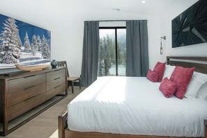 A bedroom with a large bed, a dresser, a painting of a snowy landscape, a view of a balcony with a railing, and a modern light fixture. - Big Horn House, 4387 Columbine (Vail)