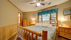 Une chambre à coucher avec un lit en bois, un ventilateur de plafond, une commode et une fenêtre avec des rideaux.