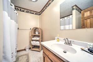 Une salle de bain avec un grand miroir, un lavabo blanc et une étagère en osier où sont posées des serviettes.