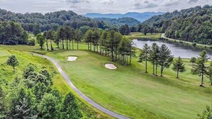 Un parcours de golf avec un lac, entouré d’arbres et de collines.
