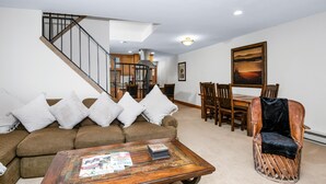 A living room with a brown sofa, a wooden coffee table, a wooden chair, a dining table with chairs, and a staircase. - Spruce Way 209, 2BD East Vail Condo (Vail)