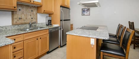 A kitchen with wooden cabinets, a stainless steel refrigerator, a coffee maker, and a dining area with chairs.
