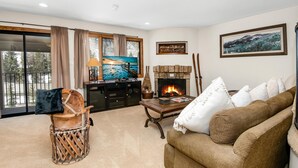 A living room with a fireplace, a television, a sofa, and a view of the outdoors. - Spruce Way 209, 2BD East Vail Condo (Vail)