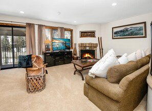 A living room with a fireplace, a television, a sofa, and a view of the outdoors. - Spruce Way 209, 2BD East Vail Condo (Vail)