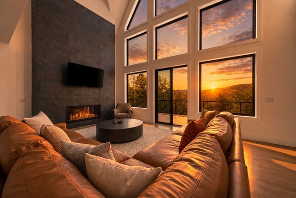 Ein modernes Wohnzimmer mit Kamin, Ledersofa und großen Fenstern mit Sonnenuntergangsblick.
