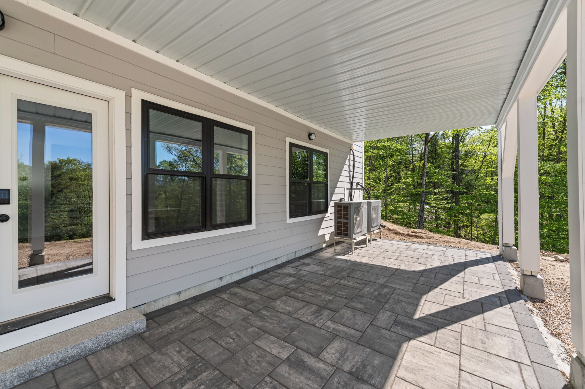 A covered outdoor area with a patio, large windows, and air conditioning units.
