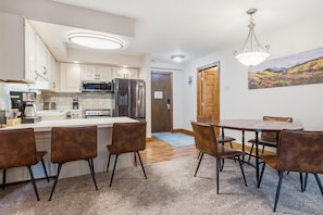 A modern kitchen with white cabinets, stainless steel appliances, and a dining area with a round table and brown chairs. - Westwind 301 2BD Gold Condo in Lionshead Village (Vail)