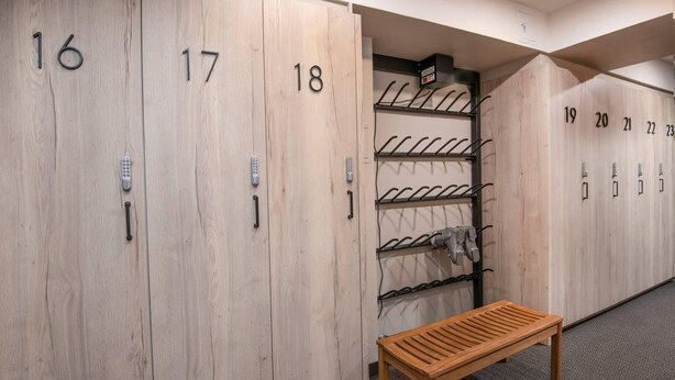 Eine Reihe von Holfachschränken mit den Nummern 16 bis 23, eine Bank und ein an der Wand befestigter Kleiderhaken.