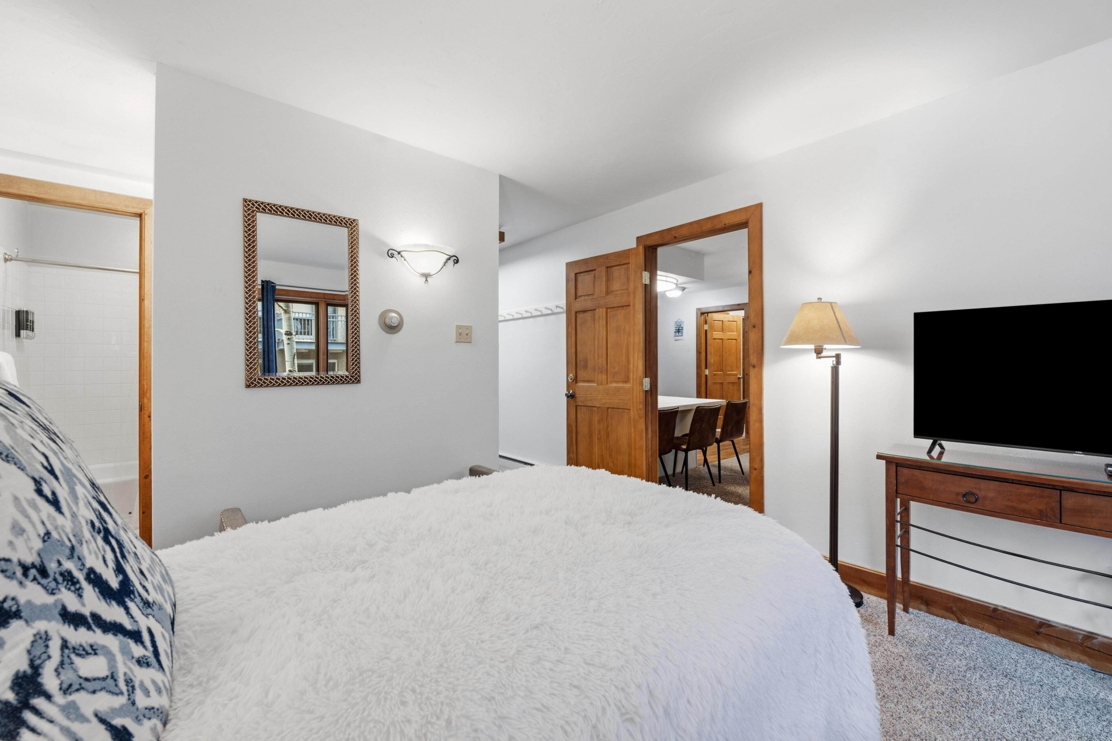 Une chambre avec un grand lit, une télévision, une lampe et une porte en bois donnant sur un coin repas.