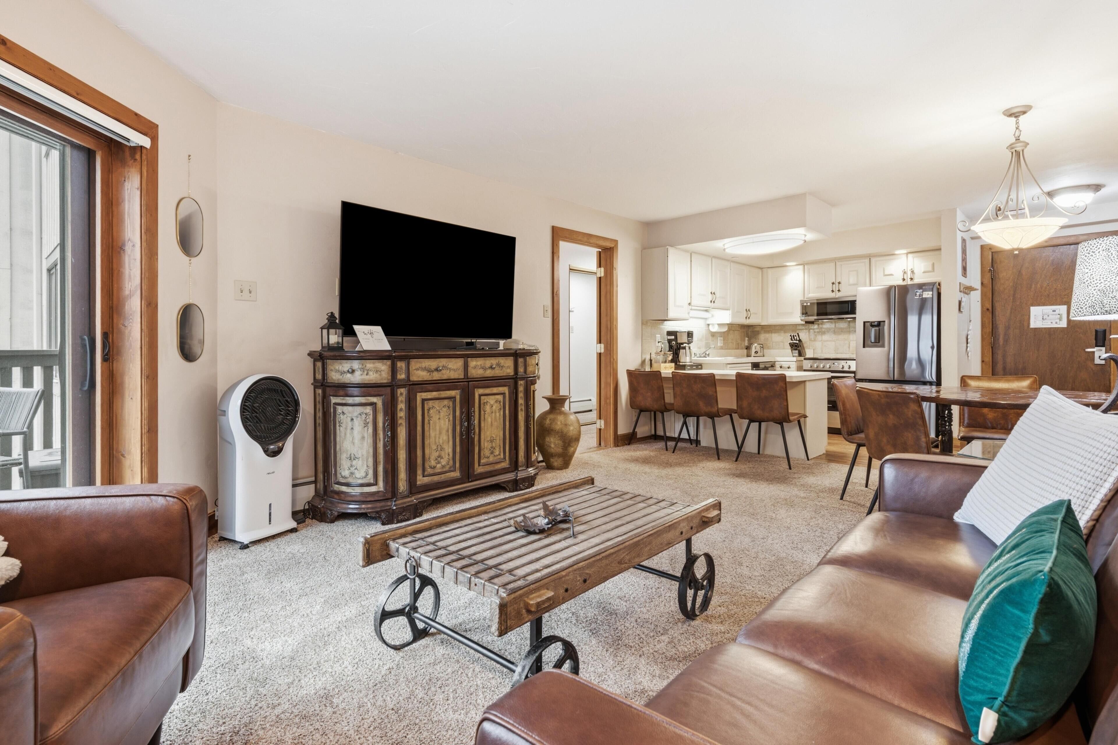 Ein Wohnzimmer mit Sofa, Couchtisch, Fernseher und einer Küche im Hintergrund.