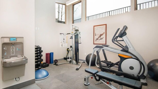 Uma academia com equipamentos de exercício, um bebedouro e um calendário na parede.