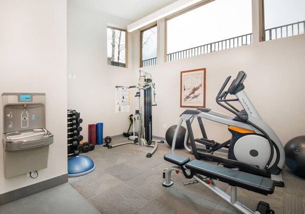 Ein Fitnessraum mit Trainingsgeräten, einem Wasserspender und einem Kalender an der Wand.