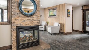 Eine Lobby mit Kamin aus Stein, weißen Sesseln, einem runden Spiegel und einem Fernseher an der Wand.