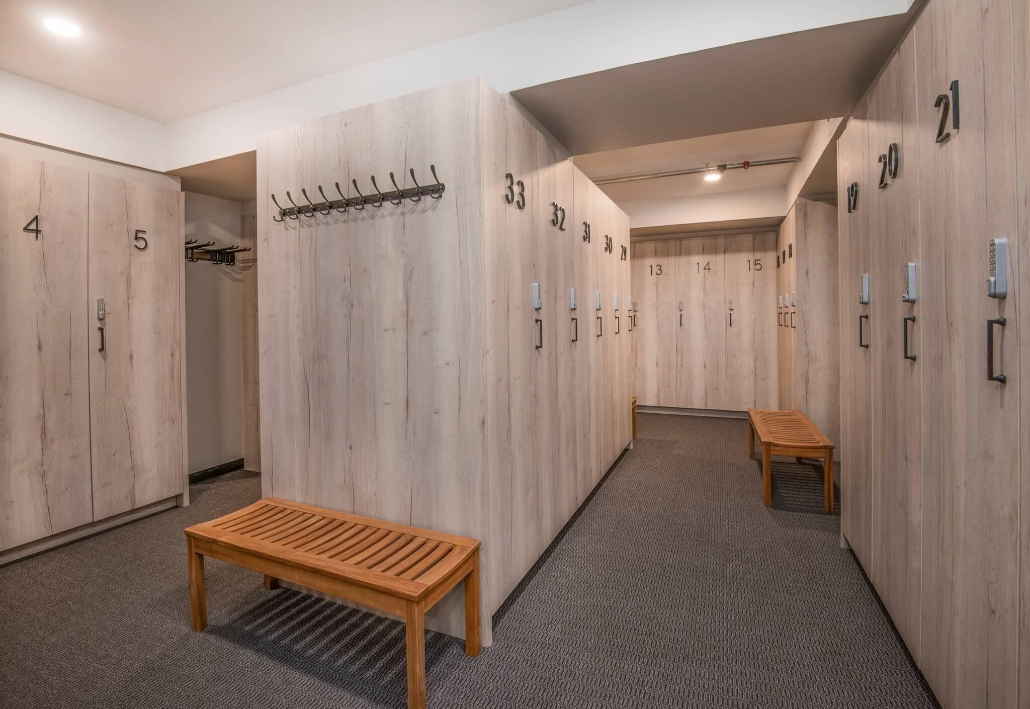 Een hotelgang met houten kluisjes genummerd van 1 tot 21, een bank en een kapstok.