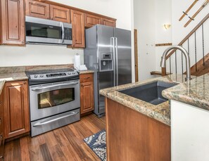 A kitchen with wooden cabinets, stainless steel appliances, granite countertops, and a wooden floor. - Timber Falls 1005, 3BD East Vail Condo With Amenities (Vail)