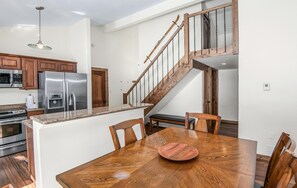 A modern kitchen with stainless steel appliances, a wooden dining table, and a staircase with wooden railings. - Timber Falls 1005, 3BD East Vail Condo With Amenities (Vail)