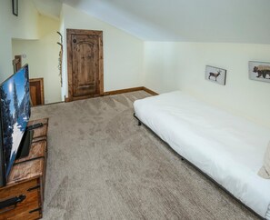 A bedroom with a bed, a wooden door, a television on a wooden stand, and a carpeted floor. - Timber Falls 1005, 3BD East Vail Condo With Amenities (Vail)