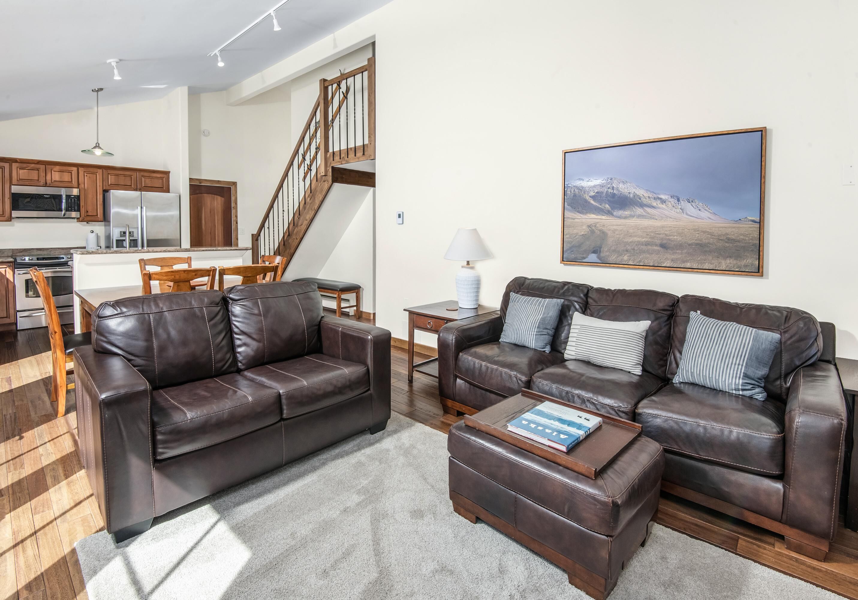 A modern living room with a brown leather sofa, a coffee table, and a painting of a mountain landscape.