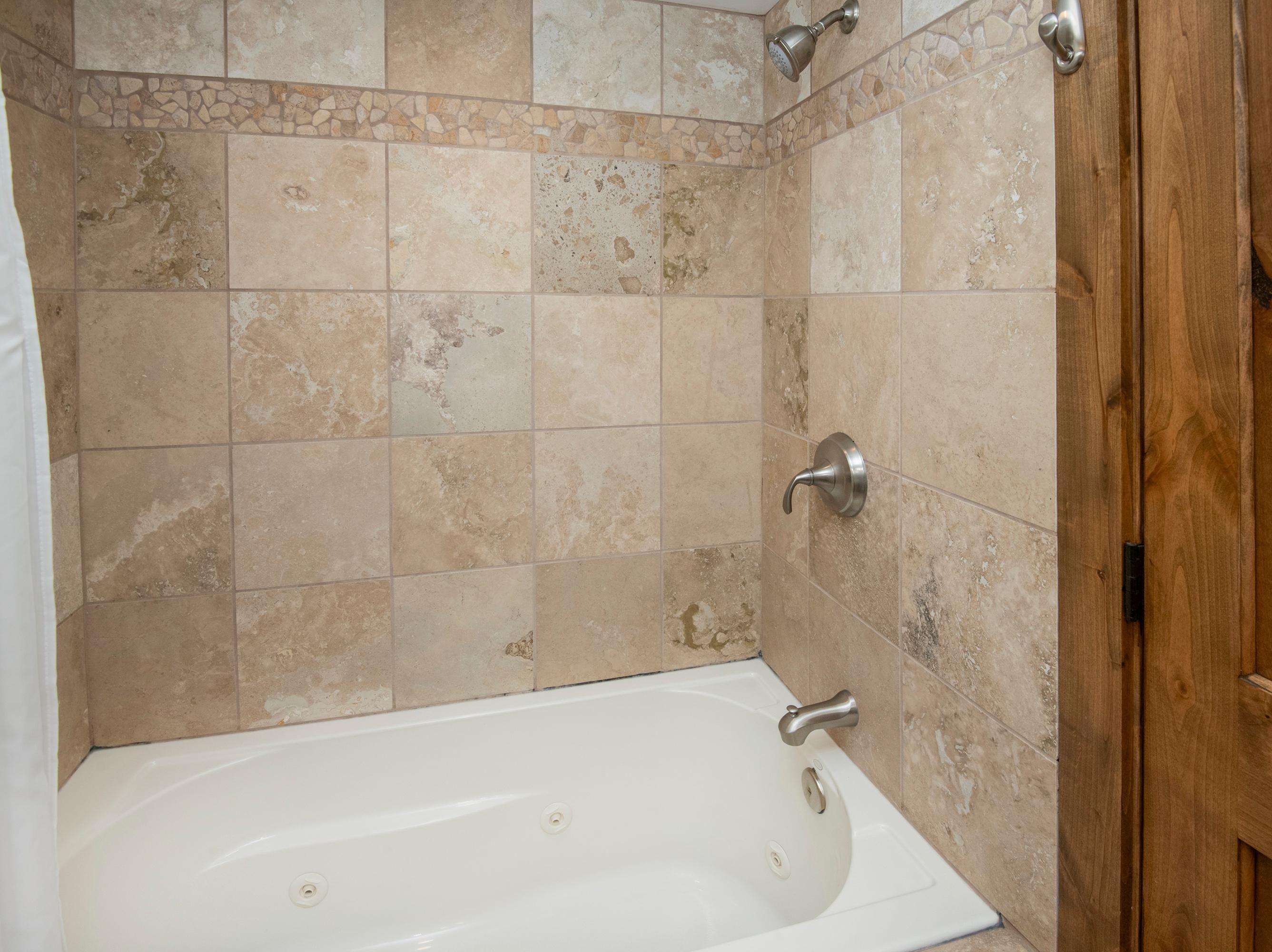 A bathroom with a bathtub, a showerhead, and a wooden door.