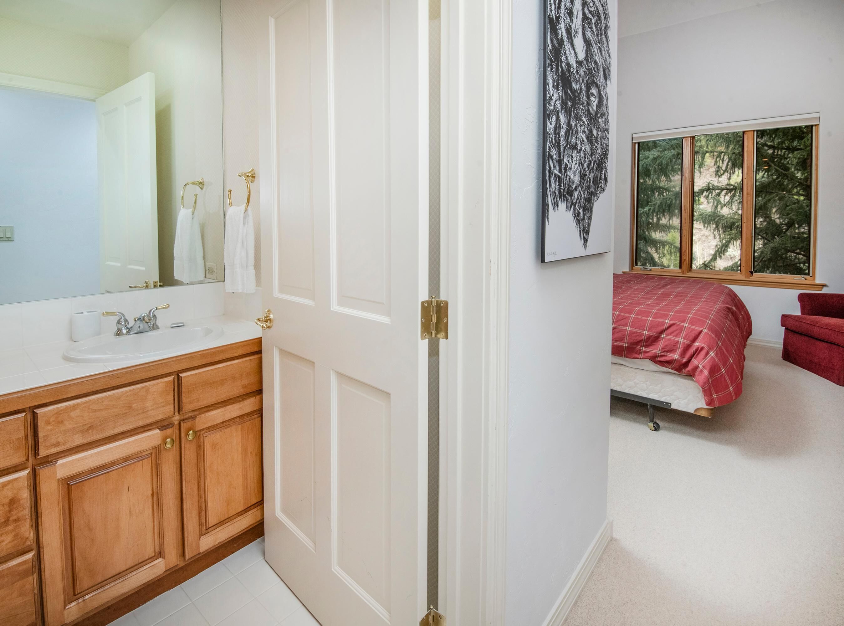 A bedroom with a bed, a window, a red chair, and a bathroom with a sink and mirror.