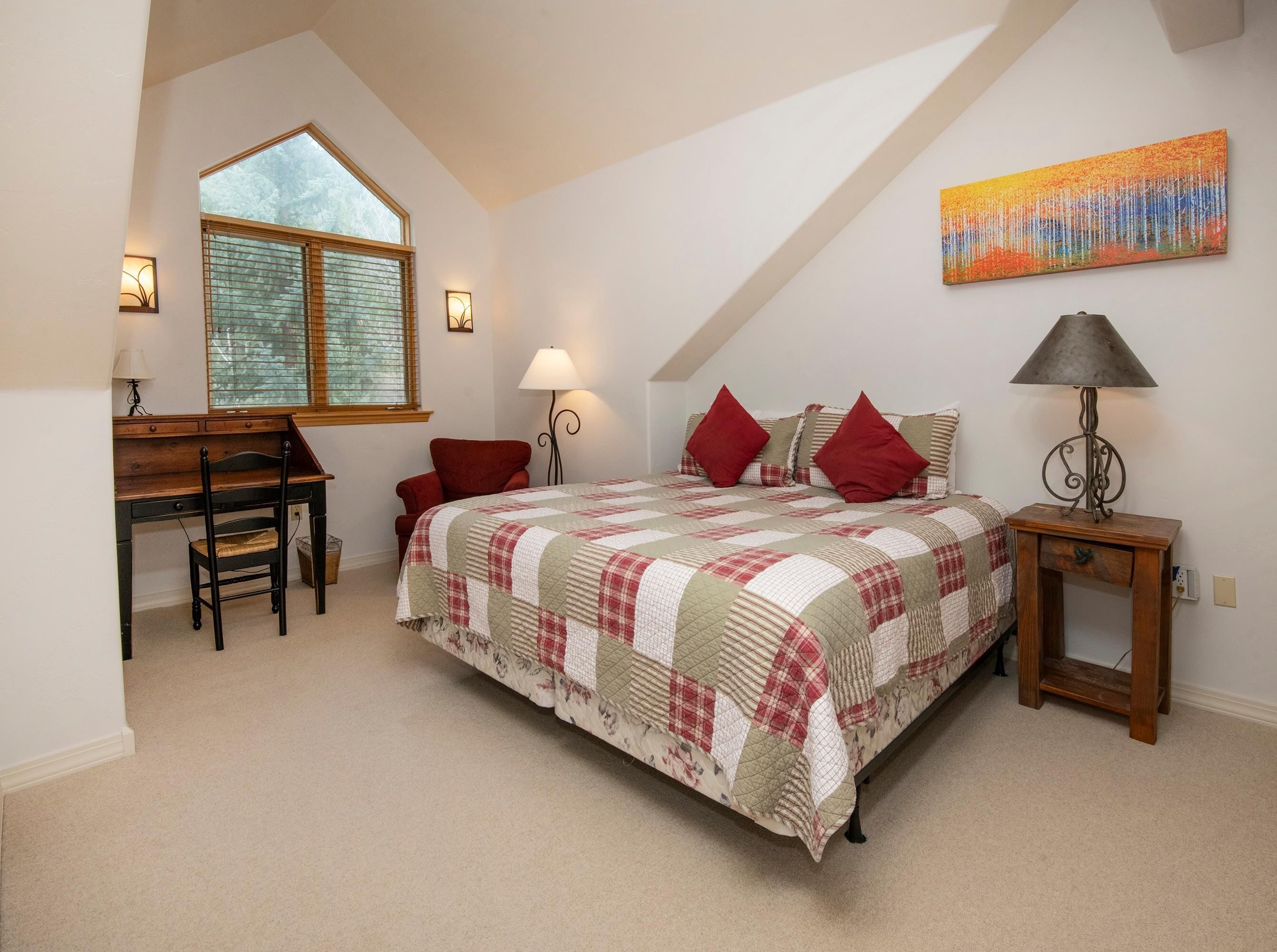 A bedroom with a bed, a desk, a chair, a lamp, and a painting on the wall.