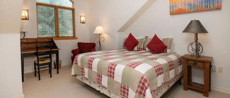 Ein Schlafzimmer mit Bett, Schreibtisch, Stuhl, Lampe und einem Bild an der Wand.