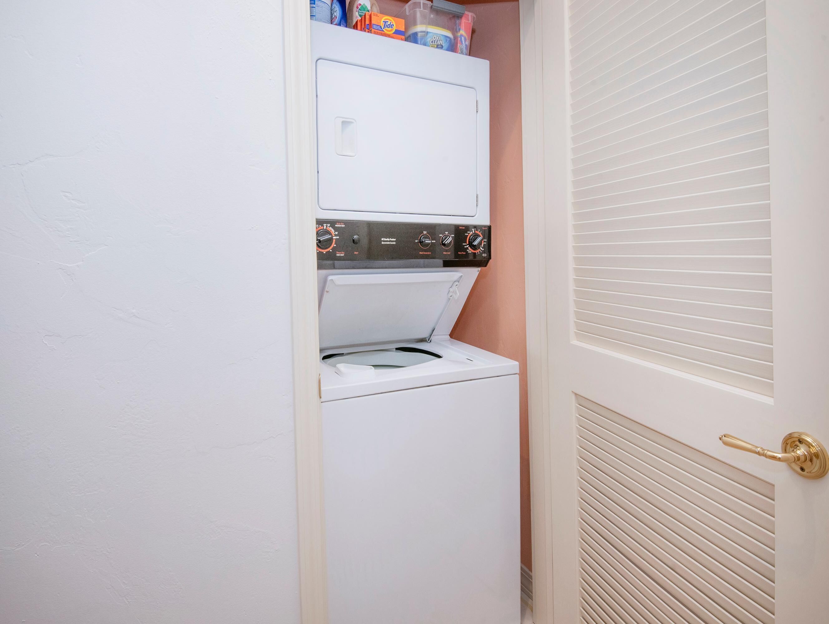 A compact laundry room with a built-in washer and dryer, a door with a brass handle, and a vent on the wall.