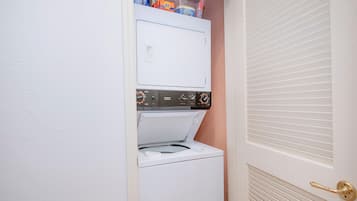 A compact laundry room with a built-in washer and dryer, a door with a brass handle, and a vent on the wall.