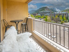 Ein Balkon mit Blick auf einen Berg, einem Tisch, zwei Stühlen und einem flauschigen weißen Teppich.