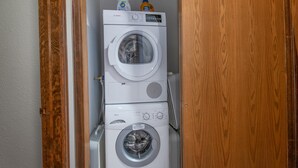 Una lavadora y secadora apiladas en un pasillo con una puerta de madera y piso de baldosas.