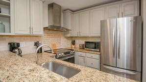 Una cocina con encimeras de granito, electrodomésticos de acero inoxidable y armarios blancos.