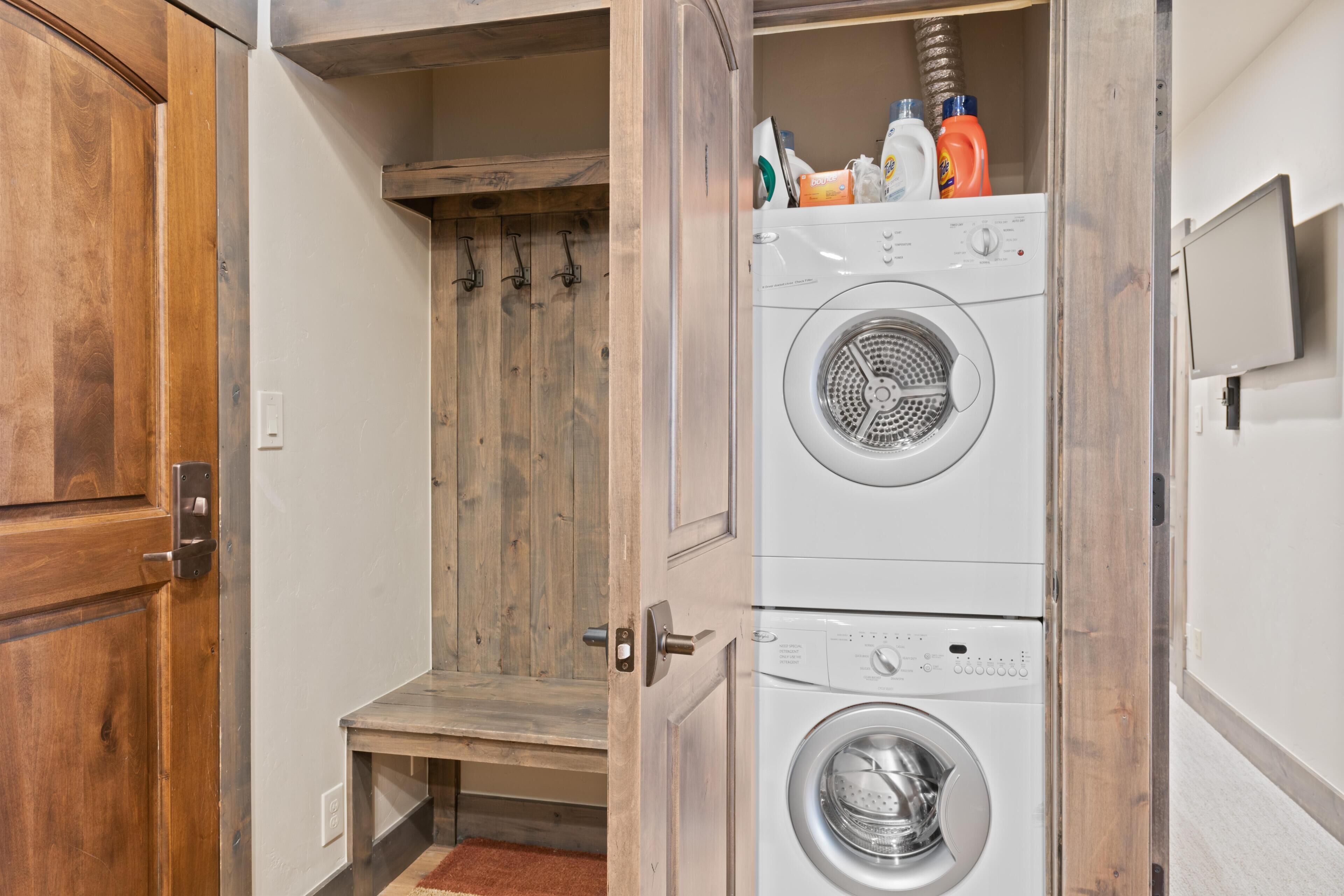 A laundry room with stacked washers and dryers, wooden cabinets, and a bench.