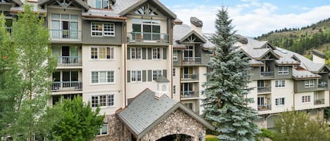 A multi-story hotel with balconies, a stone entrance, and a landscaped garden.