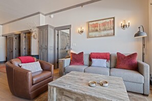 Ein Wohnzimmer mit einem braunen Ledersessel, einem grauen Sofa mit roten Kissen, einem Holztisch und einem Bild an der Wand.