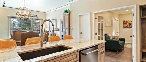 A modern kitchen with a granite countertop, stainless steel dishwasher, wooden cabinets, and a pendant light.