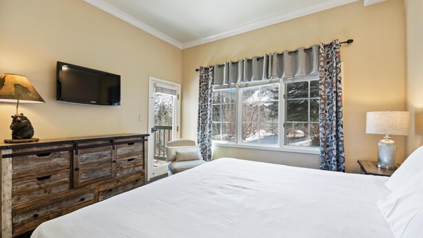 A bedroom with a bed, a TV mounted on the wall, a dresser, a chair, and a window with curtains. - Borders Lodge L108 2BD Beaver Creek Ski-in, Ski-out Condo (Avon)