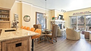 A spacious living area with a dining table, comfortable seating, a fireplace, and a large window with a view. - Borders Lodge L108 2BD Beaver Creek Ski-in, Ski-out Condo (Avon)