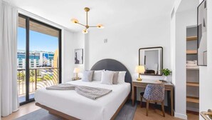 A modern hotel room with a large bed, a desk, a chair, and a balcony with a city view. - Luxury Wynwood 1BR with Rooftop Pool & Gym (Miami)