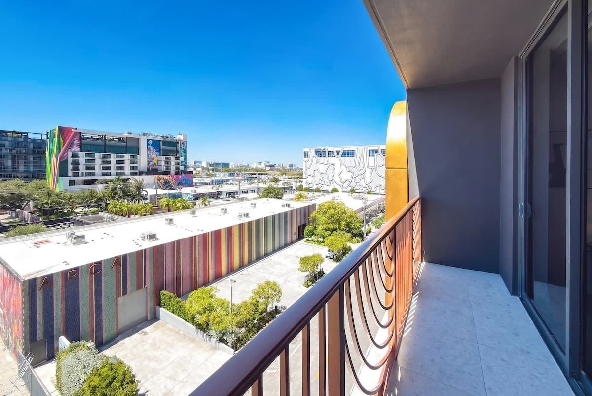 Ein Balkon mit Blick auf ein modernes Gebäude mit farbenfroher Fassade und einem darunterliegenden Parkplatz.