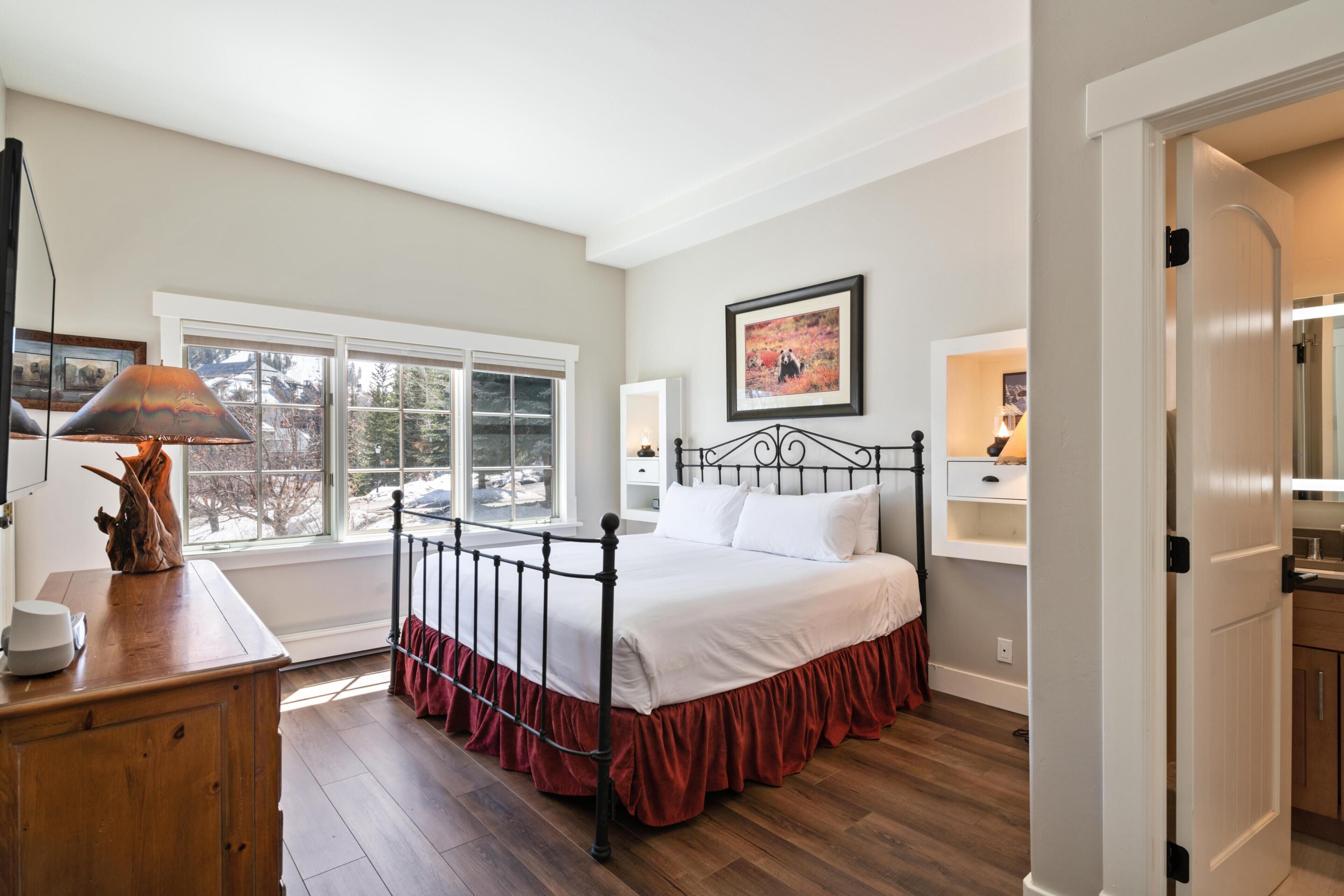 A bedroom with a bed, a dresser, a window, and a painting on the wall.