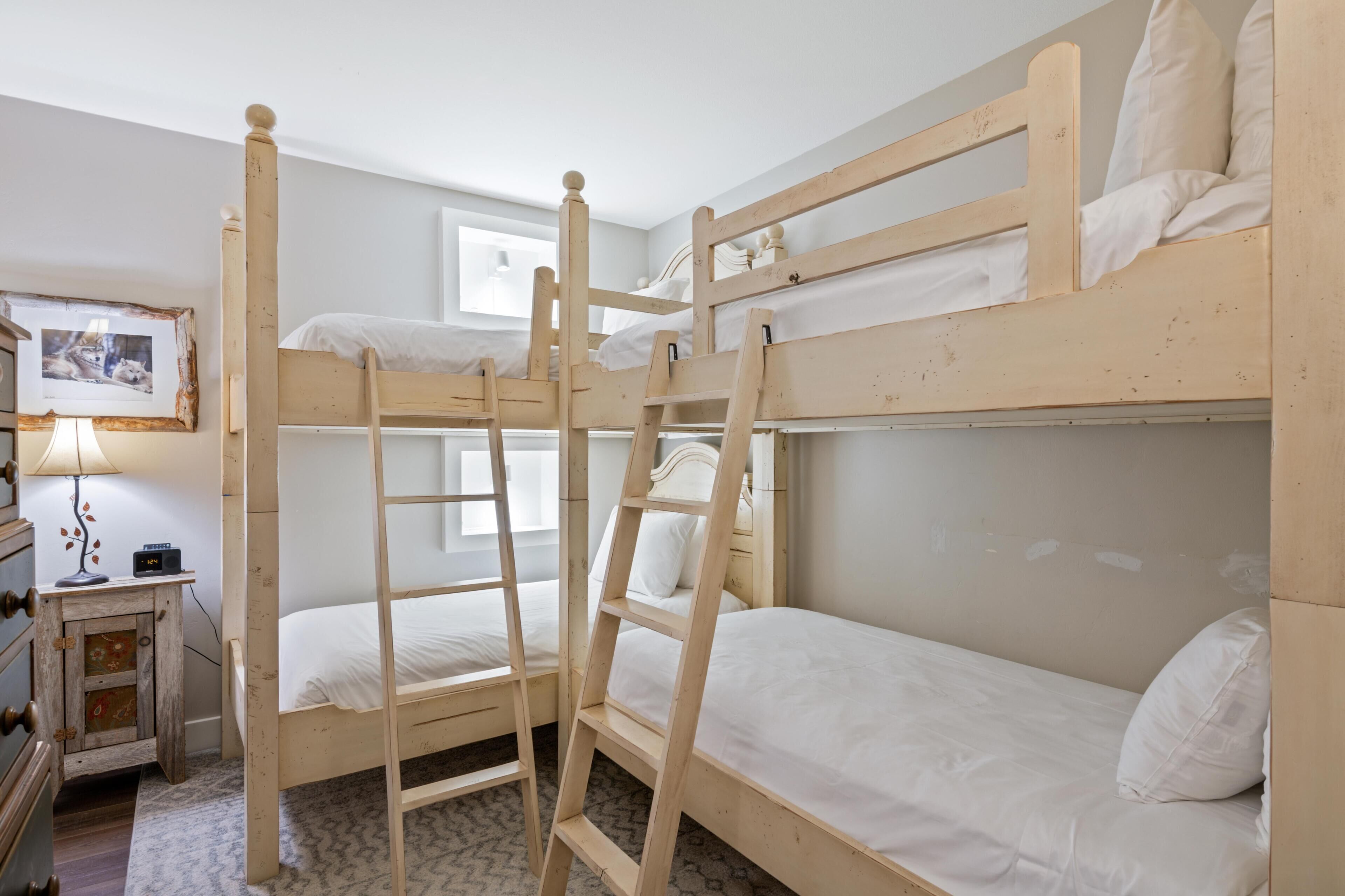 A bunk bed room with a ladder, a bedside table with a lamp, and a framed picture on the wall.