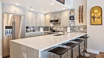 A modern kitchen with stainless steel appliances, a large island with bar stools, and a tiled backsplash.