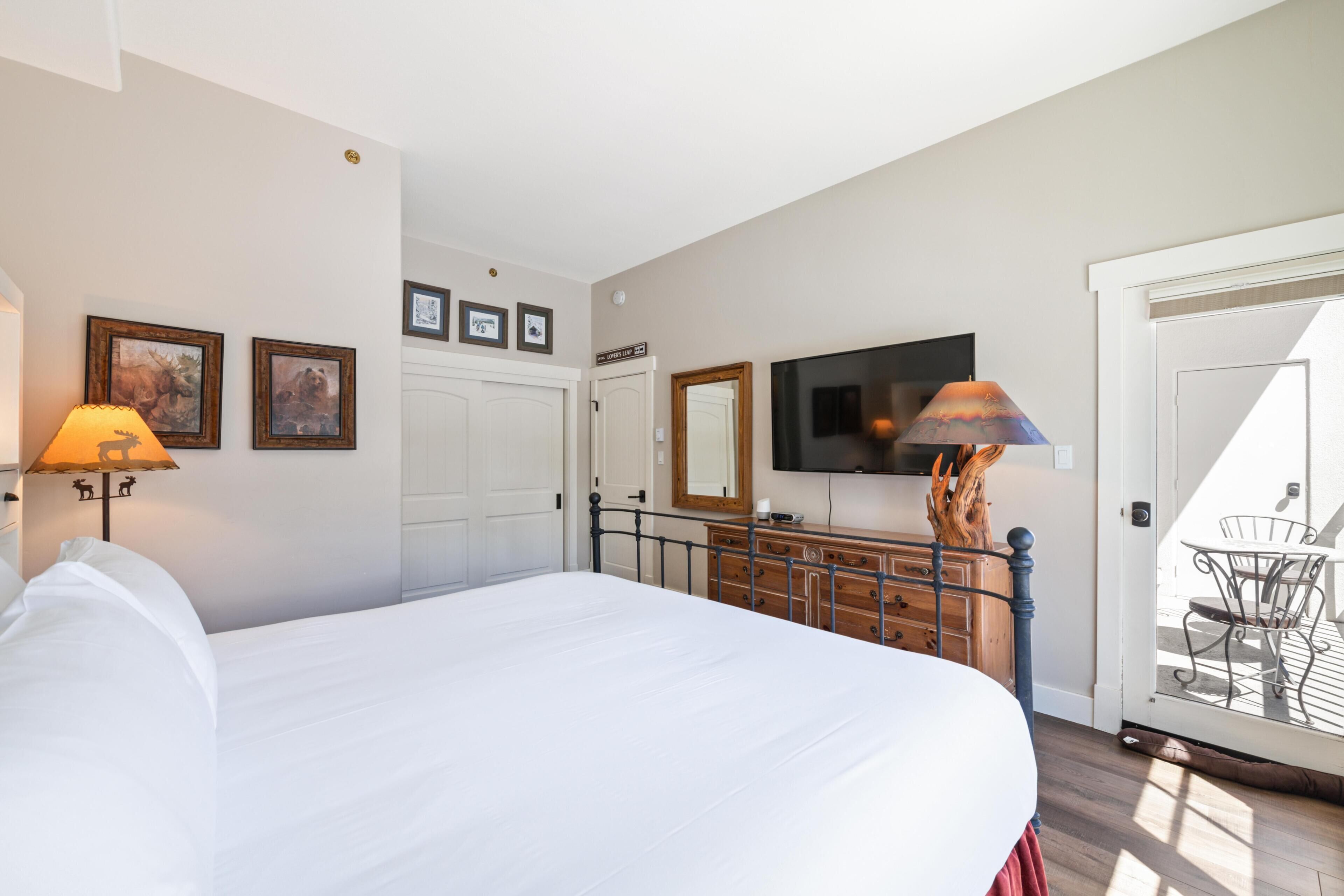 A bedroom with a bed, dresser, TV, and a door leading to a balcony.