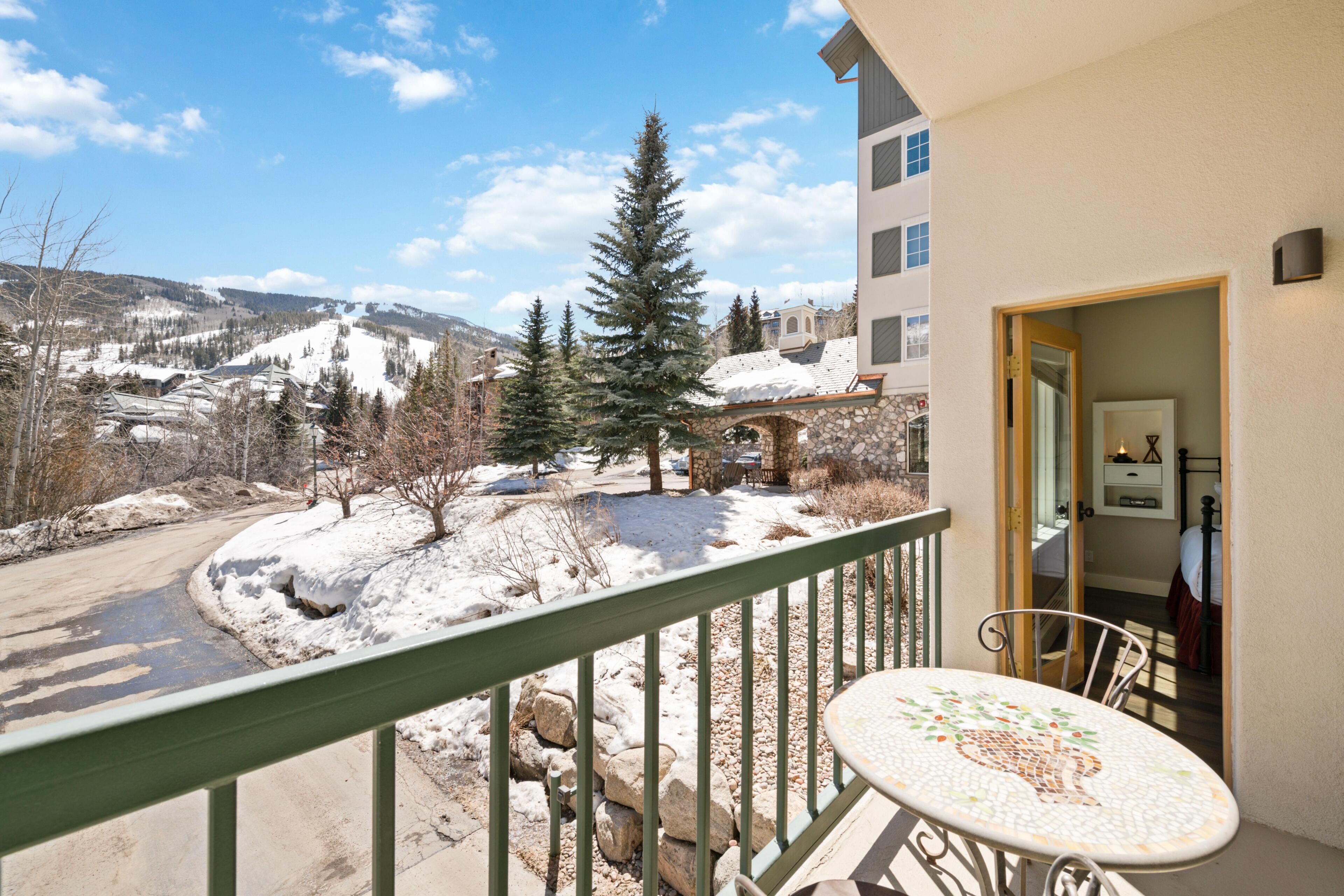 A balcony with a view of a snowy landscape, a stone building, and a table with chairs.