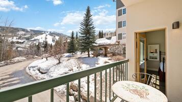 A balcony with a view of a snowy landscape, a stone building, and a table with chairs.