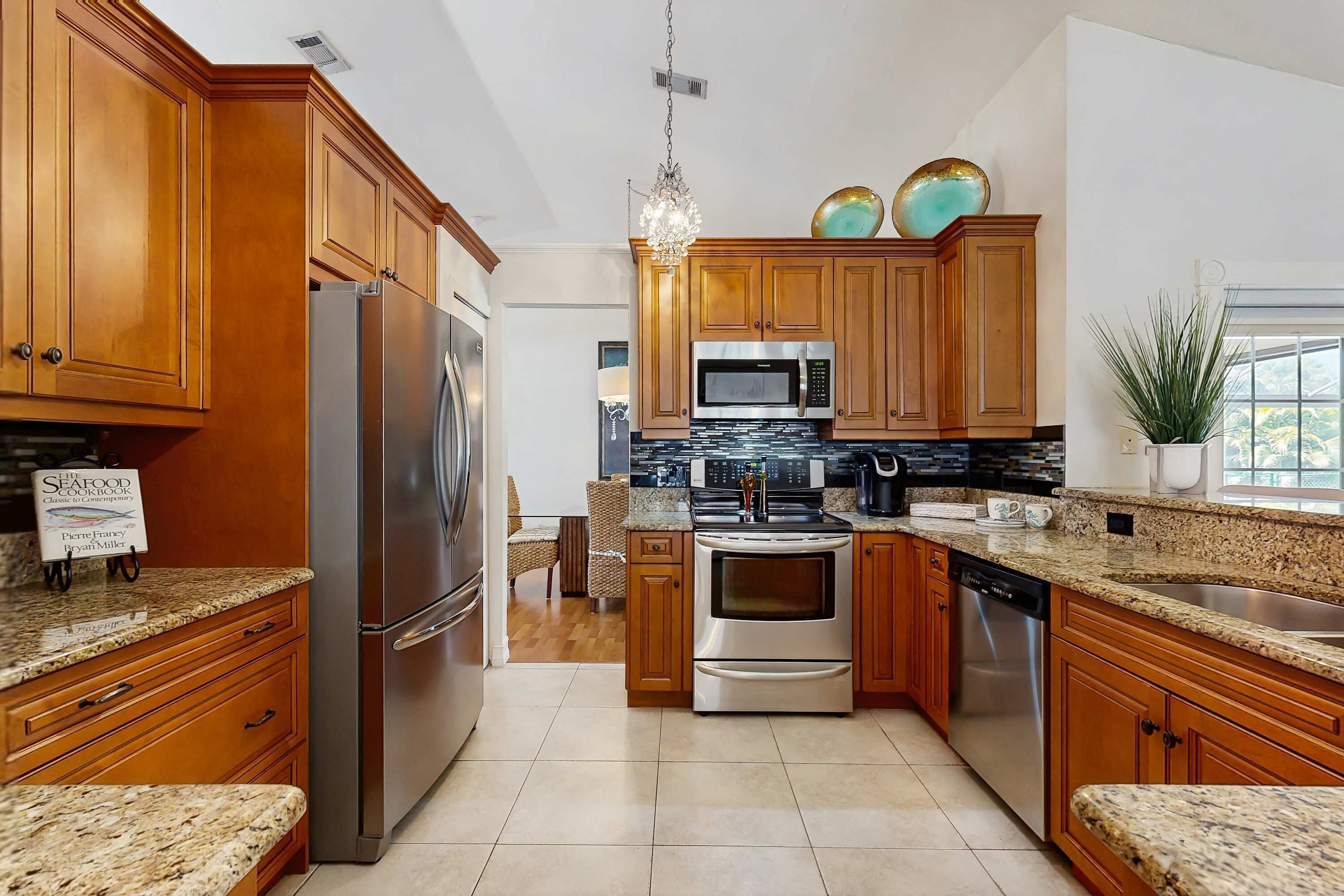 A kitchen with wooden cabinets, stainless steel appliances, granite countertops, and a chandelier.