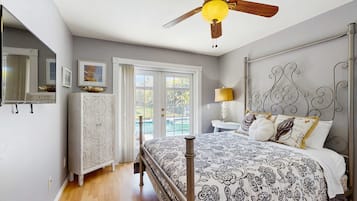 Een slaapkamer met een bed, een plafondventilator, een dressoir, een nachtkastje en een raam.