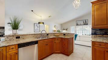 A kitchen with wooden cabinets, granite countertops, a dishwasher, and a chandelier.