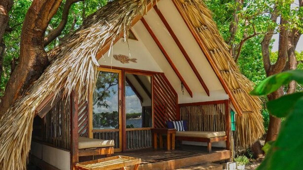 Estructura de techo de paja con terraza de madera, ventanas amplias y vista al mar.