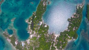 Vista aérea de una isla tropical con aguas turquesas cristalinas, vegetación verde exuberante y edificios dispersos.
